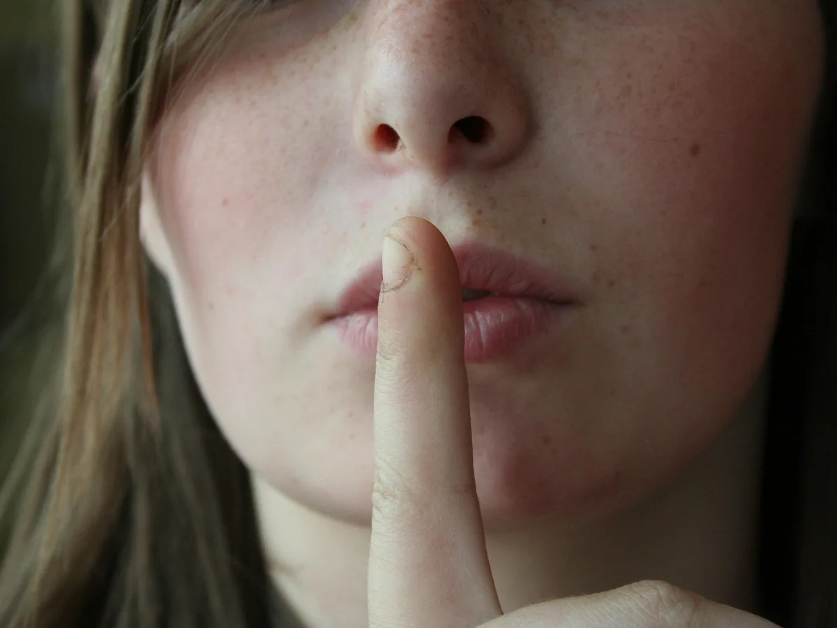 Jeune femme l'index sur les lèvres, geste du silence