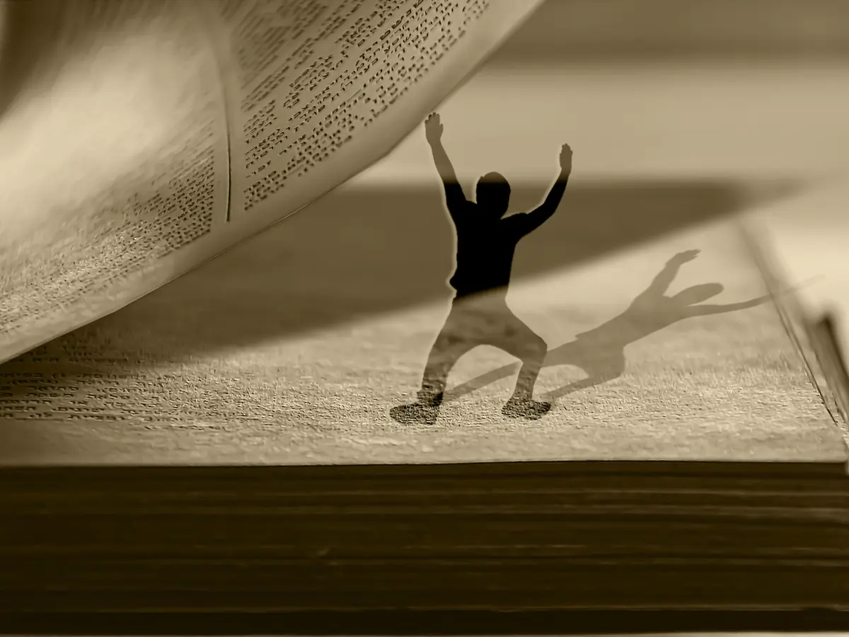 Silhouette d'un homme les bras levés sous la page d'un livre